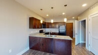 Located at 2833 Kearney Creek Ln in Lexington, KY, this single-floor unit offers a thoughtfully designed layout with consistent finishes throughout. The kitchen serves as a central highlight, featuring rich dark wood cabinetry extending to the upper walls, granite-style countertops, and wood-look flooring. A peninsula with an undermount sink and pendant lighting overhead provides both functional workspace and a natural dividing point between the kitchen and adjoining areas. Black appliances, including a refrigerator, range, and over-the-range microwave, complete the kitchen setup. Recessed lighting supplements the pendant fixtures for thorough illumination.

The bedrooms are finished with neutral-toned carpet and soft gray walls, creating a calm atmosphere. Each room is equipped with a ceiling fan and benefits from natural light through windows with views of the surrounding neighborhood. One bedroom features two closets and direct access to the bathroom, lending it a primary suite-like configuration.

The bathroom is notably spacious, finished with wood-look flooring and a granite-topped dark wood vanity. It includes accessibility features such as grab bars near the toilet and walk-in shower area, making it a practical and inclusive space. The overall layout, visible in the 3D overview, presents a compact yet functional floor plan with well-defined living zones.