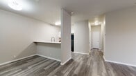 This well-designed 3-bedroom, 1-bathroom single-floor unit offers a functional and modern living experience. The open-concept layout seamlessly connects the kitchen and living room, creating a cohesive and spacious common area. The kitchen features a peninsula-style breakfast bar with a white quartz countertop, a modern pull-down faucet, white cabinetry, black appliances including a refrigerator and range, and under-cabinet range hood — all finished with durable wood-look flooring that flows throughout the entire unit.

The living room is bright and inviting, accented by a ceiling fan, built-in shelving niche, and a sliding glass door that opens to a private outdoor area, filling the space with natural light. A hallway connects the living area to the three bedrooms, each featuring the same consistent wood-look flooring and generous closet space, including a built-in rod and shelf system. The primary bedroom offers comfortable proportions and its own closet.

The shared bathroom is clean and efficiently designed, complete with a shower-tub combination, built-in open shelving, and matching flooring. Throughout the unit, neutral warm-gray tones, white trim, and consistent finishes create a cohesive, modern aesthetic that is both practical and welcoming.