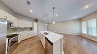 Located at 150 W Sam Houston Pkwy N in Houston, TX, this thoughtfully designed 2-bedroom, 1-bathroom residence offers a comfortable and modern living experience on a single floor. The open-concept kitchen and living area serves as the heart of the home, showcasing warm wood-look flooring, recessed lighting, and a central island with a white quartz countertop, undermount sink, and stainless steel dishwasher. The kitchen is further equipped with crisp white cabinetry, a tile backsplash, stainless steel appliances including a range and over-the-range microwave, and stylish pendant lighting above the island. The living area opens to a private balcony through a glass door, allowing natural light to fill the space. A hallway connects the main living area to the bedrooms, featuring additional storage. Both bedrooms are carpeted and bathed in natural light from sizable windows. The primary bedroom is generously sized and includes a walk-in closet with multi-level shelving and hanging rods. The full bathroom is finished with large-format tile flooring, a tiled tub/shower surround, a granite-topped vanity, and modern fixtures, creating a clean and refined aesthetic throughout.