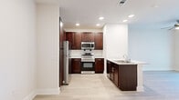 Located at 2116 N Memorial Way in Houston, TX, this one-bedroom, one-bathroom residence offers a thoughtfully designed layout across a single floor. The open kitchen and living area serves as the heart of the home, showcasing rich dark-walnut cabinetry extending to the ceiling, light-toned wood-style flooring, and a classic subway tile backsplash. The kitchen is fully equipped with a complete suite of stainless steel appliances—including a refrigerator, range, over-the-range microwave, and dishwasher—complemented by marble-style countertops and a double-basin sink. Recessed lighting throughout keeps the space bright and welcoming. The bedroom offers a comfortable, carpeted retreat with a ceiling fan, natural light from a window with blinds, and ample wall space for flexible furniture arrangements. The bathroom maintains a clean, white aesthetic with large-format tile flooring, a walk-in shower with tile surround, a dark-framed vanity mirror, a marble-style countertop, and stainless steel grab bars providing added accessibility. Additional areas with light wood flooring provide versatile utility space. The overall design balances modern finishes with a neutral palette, creating a clean and functional living environment.