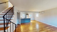 Located at 41 Wolfpit Ave in Norwalk, CT, this two-floor property offers a clean, modern aesthetic with warm hardwood flooring running throughout both levels. The upper floor features an open-concept layout where a spacious living area flows directly into the kitchen. The kitchen is well-appointed with gray shaker-style cabinetry, granite countertops, a white subway tile backsplash, and a full suite of stainless steel GE appliances including a gas range, microwave, and refrigerator. A bold teal island anchors the kitchen, adding a distinctive design element, while a wall-mounted mini-split system provides efficient climate control. Natural light fills the living space through multiple windows. A staircase with black metal railings connects the two floors. The bedrooms feature the same rich hardwood floors, large windows with blinds admitting generous natural light, and wall-mounted mini-split units. At least one bedroom offers ample closet storage with dual sliding closet doors. The bathroom is finished with wood-look tile flooring, gray vanity cabinetry, and a tub-shower combination with classic white subway tile surround. Throughout, the neutral gray wall palette and clean white trim create a cohesive, move-in-ready environment.