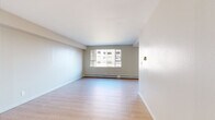 This single-floor residence offers a clean, functional layout designed for comfortable urban living. The living areas feature light hardwood-style flooring that runs throughout, complemented by neutral warm-toned walls and white ceilings that create a bright and open atmosphere. Large sliding windows in the main living spaces allow natural light to pour in while framing views of the surrounding cityscape and mature trees, adding a dynamic outdoor connection to the interior.

The galley-style kitchen is well-equipped with warm wood cabinetry, dark granite countertops, a stone tile backsplash, and a full suite of stainless steel appliances including a range, microwave, and refrigerator. Track lighting overhead provides focused illumination throughout the cooking space.

The bedrooms are finished with plush carpeting for added comfort and warmth. Each room benefits from generous window placement, with one bedroom offering a notable panoramic view of the urban skyline and autumn foliage. Mirrored sliding closet doors add a sense of depth and provide practical storage solutions.

Baseboard heating runs along the perimeter of multiple rooms, ensuring consistent warmth throughout. The overall design is understated and neutral, offering a versatile canvas well-suited to a variety of interior styles.