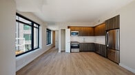 This single-floor unit is designed with a modern aesthetic, combining functionality with clean, contemporary finishes throughout. The open-concept living and kitchen area serves as the heart of the space, where light hardwood-style flooring extends seamlessly across the entire unit, creating a cohesive and airy feel.

The kitchen is a standout feature, equipped with stainless steel appliances including a range, microwave, refrigerator, and dishwasher. Dark wood-grain cabinetry spans from lower to upper sections, complemented by light stone countertops and a white subway tile backsplash. The design strikes a balanced contrast between warm and cool tones.

The living area is generously sized, benefiting from large black-framed windows that flood the space with natural light and frame elevated views of the surrounding cityscape and treetops beyond. A sliding door provides access to an additional room, offering flexibility in use.

The bedrooms feature the same hardwood-style flooring and large windows that capture scenic outdoor views, enhancing the sense of openness. The bathrooms are finished with wood-tone vanities, dark countertops, undermount sinks, and chrome fixtures, maintaining the unit's consistent modern character throughout.