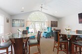Located at 730 Franklin Rd SE in Marietta, Georgia, this single-floor space offers a thoughtfully designed open layout that seamlessly connects multiple functional areas. The standout architectural feature is a dramatic arched window that anchors the sunroom area, flooding the interior with natural light and offering pleasant views of the surrounding greenery. A ceiling fan adds comfort to this bright gathering space, which is furnished with teal wingback chairs that lend a pop of color against the neutral palette.

The dining area accommodates a round glass-top pub-height table with dark wood and leather chairs, positioned near a set of French doors that open to an outdoor patio, further enhancing the connection between interior and exterior spaces. Vaulted ceilings in this section of the space contribute to an airy, open ambiance.

The living area features a comfortable beige sofa accented with teal and patterned throw pillows, complemented by a wall-mounted flat-screen television and coordinating teal cabinetry. A dedicated workspace with a desk, computer, and teal accent lamp rounds out the functional offerings of the space. Neutral carpet flooring, soft gray walls, and a textured ceiling run throughout, creating a cohesive and welcoming environment throughout the entire floor.