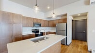Located at 2141 North McCarthy Road in Appleton, Wisconsin, this two-story, two-bedroom, two-bathroom home offers a thoughtfully designed layout across two levels. The main floor is dominated by an open-concept kitchen and living area, where warm wood cabinetry, crisp white quartz countertops, and stainless steel appliances create a functional and stylish culinary space. A large central island with a dual-basin sink serves as the focal point, accented by globe pendant lighting that adds a contemporary touch. Durable hardwood flooring runs throughout the main living areas, while a mini-split system provides climate control. The living room opens to a private balcony through sliding glass doors, offering outdoor views. Both bedrooms feature plush carpeting and ceiling fans, with the primary bedroom providing generous space and a walk-in closet with built-in shelving. The two bathrooms are well-appointed — one with a walk-in shower and warm wood vanity, the other with a full soaking tub and shower combo. A dedicated laundry room with side-by-side washer and dryer and overhead shelving adds everyday convenience. The layout also includes two hallways, two closets, and staircase access connecting both floors.