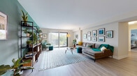 This well-appointed single-floor residence offers a thoughtfully designed layout that balances comfort and functionality. The expansive living room serves as the heart of the home, featuring light wood-style flooring, a teal accent wall, and an abundant gallery wall display. A large sliding glass door floods the space with natural light and opens to a private balcony with outdoor views, creating a seamless indoor-outdoor connection.

The galley-style kitchen is efficiently designed with two-tone cabinetry — white uppers paired with warm wood-grain lowers — complemented by white quartz countertops, a textured tile backsplash, and stainless steel appliances including a gas range and built-in microwave.

The primary bedroom offers a serene retreat with soft carpeting, a light blue accent wall, and a bright window. The second bedroom, similarly carpeted, features a bold blue accent wall and ample space for dual occupancy.

Two bathrooms serve the residence: one with a glass-enclosed walk-in shower and neutral tile finishes, and a second with a full tub-shower combination. An in-unit stacked washer and dryer adds everyday convenience, completing this well-rounded home.