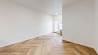Located on the third floor at 7550 N Lombard St in Portland, Oregon, this well-appointed one-bedroom, one-bathroom unit offers a clean, modern aesthetic throughout its efficiently designed layout. Warm herringbone-patterned hardwood flooring extends through the main living areas, kitchen, bedroom, and bathroom, lending a cohesive and stylish character to the entire space.

The open-concept kitchen and living room create a functional, connected environment. The kitchen features white cabinetry with brushed nickel hardware, a white quartz countertop with a classic subway tile backsplash, and a full suite of stainless steel appliances including a refrigerator, electric range, and dishwasher. A peninsula with a single-basin sink provides additional prep space and separates the kitchen from the living area. The living room benefits from natural light and direct access to a private outdoor area through glass-paned French doors.

The bedroom is a comfortable, well-proportioned room with a large window offering natural light and neighborhood views, complemented by a dedicated closet. The bathroom includes a full soaking tub and shower combination with brushed nickel fixtures. In-unit laundry adds everyday convenience, rounding out this thoughtfully designed residence.