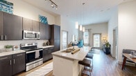 This thoughtfully designed single-floor residence offers a seamless open-concept layout that maximizes both space and functionality. The kitchen serves as a central hub, featuring dark espresso cabinetry, stainless steel appliances, subway tile backsplash, and a generous granite-topped island with an undermount double sink and bar seating — ideal for casual dining and entertaining. Elegant pendant lighting and a rail track system illuminate the space, while soaring ceilings amplify the airy atmosphere throughout.

The kitchen flows naturally into a dedicated dining area and an expansive living room, where large windows invite abundant natural light. The living area is enhanced by high ceilings and direct access to an exterior door, creating a bright and welcoming ambiance. Wood-style flooring runs throughout the main living spaces, adding warmth and continuity.

The bedrooms are carpeted for comfort and feature generous windows, ceiling fans, and ample natural light. The primary bathroom is well-appointed with a granite vanity, dark cabinetry, a soaking tub with shower, wood-style flooring, and direct access to a walk-in closet with laundry facilities nearby. An additional bathroom provides convenient access to a walk-in closet as well. This residence combines contemporary finishes with a practical, livable design.