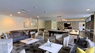 Located at 8110 Six Forks in Raleigh, North Carolina, this single-floor space is designed to impress with a refined, upscale aesthetic that balances comfort and entertainment. The main lounge area is anchored by a full-size billiards table, complemented by additional game tables that create an inviting atmosphere for recreation and socializing. Plush, curved lounge chairs in neutral tones are arranged around sleek marble-topped coffee tables, offering ample seating for guests. The flooring features a richly patterned carpet that adds depth and visual interest to the space. Overhead, recessed lighting is supplemented by elegant pendant and chandelier fixtures that cast a warm, ambient glow throughout the room. The walls are finished in a neutral palette with tasteful framed artwork, contributing to a polished, contemporary feel. A dedicated bar area is visible in the background, appointed with its own pendant lighting and cabinetry, making it well-suited for entertaining. The overall design presents a cohesive and sophisticated environment, thoughtfully curated to provide a premium social and recreational experience.