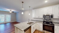 Located at 4650 Crescent Pointe Dr in North Charleston, SC, this single-floor residence offers a well-designed, open layout with a cohesive blend of modern finishes and comfortable living spaces. The kitchen serves as a central highlight, featuring crisp white shaker cabinetry, granite countertops, a large center island with a stainless steel undermount sink, and a full suite of stainless steel appliances including a refrigerator, range, microwave, and dishwasher. Stylish pendant lighting hangs above the island, adding warmth to the space. The kitchen opens seamlessly into the main living area, which is finished with rich hardwood-style flooring and features a ceiling fan and glass-paned doors leading to the exterior. Multiple bedrooms are appointed with plush wall-to-wall carpeting, ceiling fans, and windows with blinds that allow natural light to filter in. At least one bedroom includes a double-door closet for ample storage. The bathroom is cleanly finished with a granite-top vanity, white cabinetry, hardwood-style flooring, and accessibility grab bars. Throughout the home, neutral wall tones, white trim, and consistent finishes create a bright, cohesive aesthetic that is both practical and inviting.