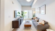 Located in the vibrant Oliver neighbourhood of Edmonton, this thoughtfully designed one-bedroom, one-bathroom unit offers a compact yet highly functional living space across a single floor. The open-concept kitchen and living area forms the heart of the unit, where light hardwood flooring flows seamlessly underfoot and an exposed concrete ceiling adds an industrial-modern character. The kitchen is outfitted with full-height two-tone cabinetry in charcoal and warm wood tones, stainless steel appliances including a built-in dishwasher, microwave, range, and refrigerator, and a clean white countertop. A bar-height dining table positioned nearby creates a practical dining zone. The adjoining living room benefits from a large sliding window that invites natural light and frames views of the surrounding urban landscape. The bedroom is a calm, well-appointed retreat featuring a sliding wardrobe, a window with outdoor views, and clean white walls. The bathroom features light hardwood-style flooring, a soaker tub with shower, and bright white fixtures accented by tasteful artwork. Throughout the unit, a neutral palette and modern finishes create a cohesive, contemporary ambiance suited for urban living.