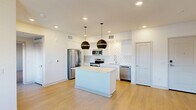 Located in Palm Desert, CA, this thoughtfully designed one-bedroom, one-bathroom residence offers a clean, modern aesthetic across a single floor. The open-concept living and kitchen area serves as the heart of the home, showcasing light hardwood flooring, recessed lighting, and an abundance of natural light from multiple windows. The kitchen is a standout feature, equipped with sleek white cabinetry, a geometric-patterned tile backsplash, stainless steel appliances including a French door refrigerator, electric range, microwave, and dishwasher, as well as a central island topped with a white quartz countertop. Two bold matte black globe pendant lights hang above the island, adding a striking contemporary touch. The living area is bright and open, with a ceiling fan and windows offering views of the surrounding neighborhood. The spacious primary bedroom is finished with plush carpeting, a ceiling fan, and windows that bring in natural light. It connects directly to a dedicated closet and a hallway leading to the full bathroom, which features a white vanity with a large mirror, wood-look flooring, and a tub-shower combination. Clean lines, neutral tones, and modern finishes create a cohesive and comfortable living environment throughout.