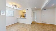 This single-floor unit presents a clean, contemporary design characterized by light hardwood flooring and crisp white walls throughout. The open-concept living area is bright and airy, benefiting from recessed lighting, a modern sputnik-style chandelier, and windows that invite natural light into the space. Exposed beams add subtle architectural interest to the ceiling.

The kitchen is efficiently designed with white subway tile backsplash, light gray shaker-style cabinetry with black hardware, white countertops, and stainless steel appliances including a refrigerator and electric range. A peninsula counter with a black matte faucet opens directly to the living area, creating a seamless flow between spaces.

The bathroom features a full tub and shower combination tiled in gray subway tile, a floating vanity with a white basin sink, black matte fixtures, and a circular mirror, all contributing to a refined, modern aesthetic.

Bedrooms are well-proportioned with continued hardwood flooring and natural light from windows. One bedroom includes a dedicated walk-in closet with built-in shelving, while ceiling fans provide additional comfort. The overall ambiance of the unit is fresh, light-filled, and move-in ready.