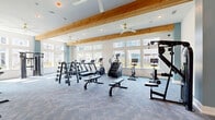 Located at 640 Lakeside Drive in Canton, Georgia, this fitness center offers a thoughtfully designed, single-floor layout divided into two complementary exercise rooms. The space is defined by its striking architectural character, featuring exposed natural wood beams, wood-paneled ceilings, and soaring ceiling heights that create an open, energizing atmosphere throughout.

The primary strength and cardio room is bathed in natural light streaming through large windows that frame views of the surrounding community. Carpeted flooring provides a sturdy foundation for a comprehensive array of equipment, including treadmills, an elliptical, a stair climber, stationary bikes, multi-station cable machines, dumbbell racks, and weight benches. Full-length mirrors amplify the sense of space while supporting proper form during workouts. Ceiling fans circulate air efficiently throughout the room.

The second exercise room transitions to smooth hardwood-style flooring, creating an ideal environment for functional training, group fitness, or yoga. This room features a rowing machine, a heavy punching bag, medicine balls, resistance equipment, and a large storage rack, all complemented by built-in low-profile shelving units for organized equipment storage. Steel-framed glass doors connect the two rooms, maintaining visual continuity while allowing each space to serve a distinct training purpose.