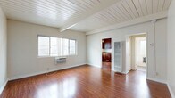 Located at 242 W Verdugo Ave in Burbank, California, this efficiently designed single-floor unit offers a well-organized layout comprising a living room, kitchen, bathroom, hallway, entrance, and two closets. The living room serves as the centerpiece of the space, showcasing rich hardwood flooring that extends throughout and a distinctive white-painted wood plank ceiling with exposed beams that add architectural character and a sense of vertical openness. A wall-mounted air conditioning unit ensures climate comfort, while a large window invites natural light and creates a bright, airy atmosphere. The kitchen is thoughtfully appointed with rich dark-wood cabinetry, granite-look countertops, a stainless steel sink, and a black gas range with an overhead exhaust hood — providing all the essentials in a compact, practical footprint. The bathroom features a clean, all-white tub and shower surround with brushed nickel hardware, maintaining a simple and functional aesthetic. Two closets offer practical storage solutions, complementing the efficient use of space throughout. The neutral color palette of soft whites and warm wood tones creates a cohesive and inviting ambiance, making this Burbank unit a functional and comfortable space.