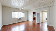 Located at 242 W Verdugo Ave in Burbank, California, this efficiently designed single-floor unit offers a well-organized layout comprising a living room, kitchen, bathroom, hallway, entrance, and two closets. The living room serves as the centerpiece of the space, showcasing rich hardwood flooring that extends throughout and a distinctive white-painted wood plank ceiling with exposed beams that add architectural character and a sense of vertical openness. A wall-mounted air conditioning unit ensures climate comfort, while a large window invites natural light and creates a bright, airy atmosphere. The kitchen is thoughtfully appointed with rich dark-wood cabinetry, granite-look countertops, a stainless steel sink, and a black gas range with an overhead exhaust hood — providing all the essentials in a compact, practical footprint. The bathroom features a clean, all-white tub and shower surround with brushed nickel hardware, maintaining a simple and functional aesthetic. Two closets offer practical storage solutions, complementing the efficient use of space throughout. The neutral color palette of soft whites and warm wood tones creates a cohesive and inviting ambiance, making this Burbank unit a functional and comfortable space.
