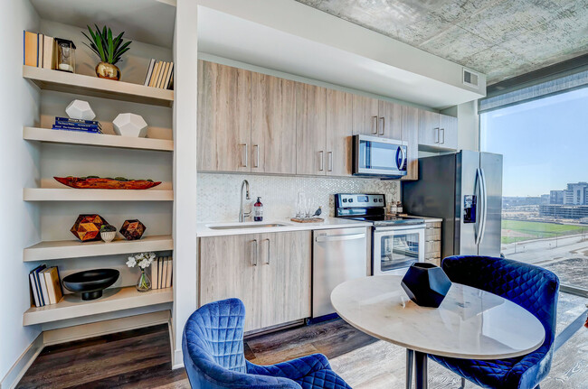 Impresionante cocina y sala de estar de concepto abierto con electrodomésticos de acero inoxidable, pisos de madera de tablones, iluminación colgante y encimeras de cuarzo - SkyHouse Frisco Station