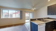 Located at 9603 NE Hazel Dell Ave in Vancouver, Washington, this single-floor unit offers a well-organized layout with functional living spaces throughout. The kitchen serves as a central highlight, featuring a peninsula with granite-style countertops, a mosaic tile backsplash, dark espresso cabinetry extending to the ceiling, and white appliances including a range and refrigerator. The peninsula opens directly to the living area, creating a connected, open feel. The living room benefits from natural light streaming through a large window and sliding glass door that leads to an outdoor patio, while a ceiling fan adds comfort overhead. Soft carpeting flows through the living room and into the bedrooms, each of which includes a ceiling fan and access to natural light via windows. The primary bedroom connects to a private bathroom with a vanity, granite-topped cabinetry, lighted mirror, and hardwood-style flooring. A second full bathroom features a clean tub and shower combination with wood-look floors. Closet space is accessible via sliding doors, and the vaulted ceiling heights in select areas lend a sense of openness throughout the unit.