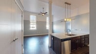 This thoughtfully designed one-bedroom, one-bathroom unit offers a comfortable and functional layout across a single floor. The open-concept living and kitchen area is anchored by impressively high ceilings and dark hardwood flooring that runs throughout, creating a cohesive and polished aesthetic.

The kitchen is a standout feature, equipped with a full suite of stainless steel appliances including a refrigerator, range, and built-in microwave. Rich dark cabinetry reaches toward the ceiling, providing ample storage, while the expansive quartz peninsula with an undermount sink serves as both a workspace and casual dining area. Pendant lighting in amber glass adds a warm, stylish accent above the peninsula.

The living room benefits from elevated ceilings and dual windows that invite natural light into the space, complemented by a ceiling fan for added comfort. The two-tone blue-gray and white wall treatment carries throughout, lending a calm, modern character to every room.

The bedroom is generously sized, featuring multiple windows with roll-down shades and the same hardwood flooring. Two closets provide practical storage. The bathroom includes a clean, fully tiled walk-in shower with a rainfall-style fixture. The unit also includes a dishwasher and in-unit storage solutions for everyday convenience.