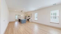 Located at 1035 Brightwater Way in Calabash, NC, this thoughtfully designed single-story home offers a bright, modern interior with a clean neutral palette and light-toned hardwood flooring throughout the main living areas. The heart of the home is an open-concept dining, kitchen, and living space that creates a seamless flow for everyday living and entertaining. The kitchen is a standout, featuring a large center island with a white quartz countertop and a two-toned gray base, cream cabinetry with gold hardware, stainless steel appliances, and a wood-beam pendant light fixture above the island. A stylish barn door adds a contemporary farmhouse touch. The den offers additional flexible living space with multiple windows that invite generous natural light and outdoor views of the surrounding greenery. The bedroom features plush carpeting, a ceiling fan, and windows overlooking the yard. An en-suite bathroom is finished with light wood-look tile flooring, a white vanity with gold fixtures, a walk-in glass shower, and a bright window. A dedicated laundry room houses a full-size washer and dryer with overhead shelving. Three closets and a utility room provide ample storage throughout this well-appointed home.
