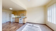 This efficient one-bedroom, one-bathroom unit is thoughtfully laid out across a single floor, making smart use of every square foot. The kitchen anchors one end of the main living area, featuring light maple cabinetry with ample upper and lower storage, a full suite of white appliances including a refrigerator, electric range, dishwasher, and an under-cabinet range hood. Countertops provide functional prep space, and a stainless steel sink sits beneath a window, allowing natural light to fill the work area. The kitchen flows seamlessly into the open living space, which is finished with durable hardwood-style flooring and topped with a ceiling fan—ideal for comfort year-round. A large window at the far end of the living area bathes the space in natural light. The bedroom is a quiet, carpeted retreat with soft, neutral tones and a closet offering built-in shelving and hanging rods for organized storage. The bathroom is clean and functional, featuring a light wood vanity with under-sink storage, a large mirror, and a combination tub and shower. Hardwood-style flooring continues here, tying together the unit's cohesive aesthetic. Warm cream-toned walls throughout lend the space a bright, welcoming atmosphere.