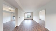 This thoughtfully designed 2-bedroom, 2-bathroom residence offers a clean, contemporary aesthetic throughout its single-floor layout. Rich hardwood-style flooring flows continuously through the open-concept living and kitchen area, anchoring the bright, neutral-toned interior. The kitchen is outfitted with stainless steel appliances including a range, dishwasher, and refrigerator, complemented by modern grey cabinetry, a sleek countertop island with a pendant light, and under-cabinet lighting that adds warmth and functionality. The living area is bathed in natural light through large framed windows fitted with roller shades, offering pleasant outdoor views. Each bedroom is well-proportioned, with the primary bedroom featuring a sliding-panel closet for streamlined storage. Both bathrooms are finished with light tile flooring and clean white fixtures; one includes a soaking tub with full-height tile surround and chrome hardware, while the other features a white vanity with under-sink storage and modern vanity lighting. A dedicated laundry closet houses a stacked washer and dryer unit for added convenience. The hallway connects all spaces efficiently, maintaining an organized and cohesive flow throughout the residence.