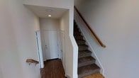 This two-bedroom, three-bathroom townhouse is thoughtfully arranged across three floors, providing a well-defined separation of living spaces. The entry level welcomes residents with a clean, minimalist foyer featuring rich dark hardwood flooring and a recessed ceiling light that illuminates the entryway. A louvered closet door offers convenient storage at the entrance, while a solid white front door with secure hardware provides a welcoming threshold. Carpeted stairs with a warm wood handrail rise from the entry, connecting the floors and hinting at the multi-level layout within. The neutral white walls throughout create a bright and airy atmosphere, lending a versatile backdrop suitable for a variety of interior styles. The staircase serves as a central architectural element, efficiently linking each level and allowing each floor to function as its own distinct zone. With three full bathrooms distributed across the home, residents and guests alike benefit from added convenience and privacy. The townhouse layout is ideal for those seeking defined living, sleeping, and utility areas spread across multiple levels, making efficient use of vertical space while maintaining a comfortable and organized living environment.