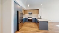 Located at 18750 Delaware St in Huntington Beach, California, this thoughtfully designed one-bedroom, one-bathroom residence offers a well-organized layout across a single floor. Warm-toned hardwood flooring flows consistently throughout every room, unifying the space with a clean, contemporary aesthetic.

The kitchen is a standout feature, showcasing bold slate-blue lower cabinetry paired with natural wood upper cabinets and crisp white countertops. Stainless steel appliances — including a gas range, microwave, refrigerator, and dishwasher — complete the fully equipped culinary space. A peninsula with an integrated sink provides additional prep and dining space, making the kitchen both functional and visually striking.

The bedroom is a calm, light-filled retreat with white walls and a window that invites natural light. A closet with louvered doors adds practical storage, while the room's clean lines contribute to a serene atmosphere.

The bathroom continues the modern design language with blue cabinetry, a white quartz vanity, a large mirror, recessed lighting, and a full-sized soaking tub with tiled surround. A hallway connects the rooms seamlessly, and the private balcony extends the living space outdoors — a welcome amenity in sunny Southern California.