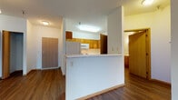 This single-floor residential unit offers a well-organized and functional layout designed for comfortable everyday living. The open-concept kitchen is equipped with warm honey-toned oak cabinetry, white appliances including a range, microwave, dishwasher, and refrigerator, complemented by light countertops and hardwood-style flooring. A built-in peninsula with a breakfast bar separates the kitchen from the living area, creating a natural flow between spaces. The entry foyer opens directly to the living area, which features rich, dark hardwood-style flooring and a pendant light fixture. A dedicated in-unit laundry area with a full-size washer and dryer is conveniently tucked near the entry. The bedrooms are carpeted and bright, each featuring windows with outdoor views of surrounding greenery, providing natural light and a calm atmosphere. The unit includes two bathrooms: a full bath with a tub/shower combination, wood-toned vanity, and large mirror, and a second bath featuring a walk-in shower stall alongside built-in shelving for additional storage. Warm wood trim and baseboards are consistent throughout, unifying the design across all rooms. This unit balances practicality with a cohesive, understated aesthetic suitable for a variety of lifestyles.