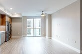 This single-floor residence showcases a thoughtfully designed open-concept layout with a neutral color palette and light wood-look flooring that flows seamlessly throughout. The living area is generously proportioned, featuring a ceiling fan, recessed lighting, and large floor-to-ceiling windows that draw in ample natural light while offering views of the surrounding building exterior.

The kitchen is a standout feature, outfitted with warm wood cabinetry extending to the ceiling, a textured geometric tile backsplash, white countertops, and a full suite of stainless steel appliances including a gas cooktop, wall oven, built-in microwave, dishwasher, and a French door refrigerator. A range hood and under-cabinet lighting add both function and style.

The bedroom features a large sliding glass door that brightens the space with natural light, while an adjacent walk-in closet offers multi-level hanging rods and generous storage capacity. The bathroom is finished with large-format marble-look tile in the tub surround, complemented by neutral wall tones and tile flooring. Throughout the unit, clean lines, modern finishes, and an open flow create a cohesive and functional living environment.