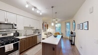 Located at 98 N 1st St in the heart of downtown San Jose, this thoughtfully designed one-bedroom, one-bathroom residence offers an efficient and comfortable layout across a single floor. The open kitchen is a standout feature, showcasing rich wood cabinetry paired with crisp white upper cabinets, quartz countertops, a mosaic tile backsplash, and a full suite of stainless steel appliances including a gas range, microwave, dishwasher, and French door refrigerator. A central island with pendant lighting adds both prep space and visual appeal. In-unit stacked laundry is conveniently accessible near the kitchen entry. The living room offers a warm, inviting atmosphere with hardwood-style flooring, a ceiling fan, and a window that brings in natural light. The bedroom features plush carpeting, a ceiling fan, and direct access to a dedicated walk-in closet with built-in shelving. The bathroom is finished with large-format tile flooring, a soaking tub and shower combo with subway tile surround, a dark wood vanity with ample cabinetry, and a wall-mounted storage cabinet. Clean white walls and modern finishes throughout create a cohesive, contemporary aesthetic suited for urban living.