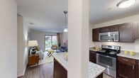 This thoughtfully designed one-bedroom, one-bathroom residence in Northville, Michigan offers a comfortable and functional layout across a single floor. The open-concept kitchen and living area form the heart of the unit, creating a seamless flow between spaces. The kitchen is well-equipped with rich dark-wood cabinetry, granite countertops, stainless steel appliances including a refrigerator, range, microwave, and dishwasher, and a peninsula that doubles as a casual dining or prep surface, illuminated by pendant lighting overhead. Wood-style flooring runs throughout the main living area, adding warmth and continuity.

The living room is bright and inviting, benefiting from a sliding glass door that fills the space with natural light and provides views of the outdoor surroundings. The bedroom features plush carpeting, multiple windows with outdoor views, and ample space for furnishings. A dedicated closet and hallway provide practical storage. The bathroom is finished with granite countertops, dark cabinetry, a tiled tub-shower combination, and decorative wallcovering, rounding out this well-appointed residence.
