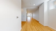 Located at 101 South Salina Street in the heart of downtown Syracuse, New York, this single-floor unit offers a thoughtfully designed, modern living space with a clean, contemporary aesthetic. The open floor plan flows seamlessly from one end to the other, creating a bright and airy atmosphere enhanced by recessed lighting and warm-toned hardwood flooring throughout the main areas.

The kitchen is a standout feature, outfitted with white shaker-style cabinetry, light countertops, a subway tile backsplash, and a full suite of stainless steel appliances including a refrigerator, range, microwave, and dishwasher. The layout places the kitchen along one wall, allowing it to integrate naturally into the open living space without interruption.

The expansive main living area stretches toward a window at the far end, allowing natural light to filter in and offering views of the surrounding downtown Syracuse skyline. Structural columns punctuate the space, adding an architectural element consistent with the building's urban character.

The bathroom is finished with large-format tile flooring and features accessibility-conscious details, including grab bars and a wide door clearance, reflecting a practical and inclusive design approach. The crisp white walls throughout the unit maintain a neutral, versatile backdrop suitable for a variety of uses.