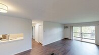 Located at 1049 S Main St in Crown Point, Indiana, this 2-bedroom, 2-bathroom unit offers a well-organized single-floor layout designed for comfortable everyday living. The living room is a highlight of the space, featuring rich dark hardwood flooring, a wall-mounted air conditioning unit, and a sliding glass door that opens to a private balcony with an outdoor railing — bringing in abundant natural light and views of surrounding greenery. An interior pass-through window connects the living area to the kitchen, adding an open, communicative feel between spaces. Both bedrooms are carpeted and generously proportioned, each offering windows with natural light and baseboard heating. The primary bedroom also includes a wall-mounted air conditioning unit for added climate control. The two bathrooms are thoughtfully updated: one features a clean, modern vanity with a speckled quartz countertop, an undermount sink, and elegant pendant lighting above a large mirror, while the second showcases a classic subway tile tub surround with a built-in niche and brushed hardware. Additional features include a dedicated closet, a connecting hallway, and durable dark hardwood flooring in the main living areas. The overall aesthetic is clean and neutral, offering a move-in ready canvas throughout.