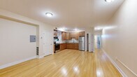 This single-floor residence offers a practical and comfortable layout with two bedrooms, one bathroom, and a combined kitchen and living area. The open-plan kitchen and living room is anchored by warm light hardwood flooring that extends throughout the main living spaces, creating a bright and cohesive atmosphere. The kitchen is well-equipped with warm-toned wood cabinetry, light stone-finish countertops, stainless steel appliances including a refrigerator, range, and microwave, and a double sink — all arranged in an efficient L-shaped configuration. A walk-in closet is conveniently accessible directly from the kitchen area. The spacious primary bedroom features plush carpeting, dual windows that invite natural light, and a closet, providing a comfortable and serene retreat. The second bedroom mirrors this design with carpet flooring, additional windows, and a closet of its own. The full bathroom is finished with neutral tile throughout the tub/shower surround and floor, complemented by a glass-block window above the tub that allows in diffused natural light. Throughout the residence, neutral warm-beige wall tones and clean white trim create a calm, move-in-ready aesthetic that suits a variety of interior styles.