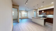 This two-story residence offers a thoughtfully designed layout across two floors, with the majority of the living space situated on the upper level. The open-concept main living area seamlessly connects the kitchen and living room, featuring light hardwood-style flooring, crown molding, track lighting, and a ceiling fan. Large windows invite abundant natural light and provide outdoor views, while a door leads to a private balcony. The kitchen is well-equipped with rich dark wood cabinetry, granite countertops, stainless steel appliances, a tile backsplash, and a peninsula with pendant lighting that offers additional prep and bar seating space. Built-in open shelving extends the kitchen's storage and display options. The primary bedroom is generously sized and includes a walk-in closet with built-in shelving and a full en-suite bathroom featuring a double vanity with granite countertops, a soaking tub, a separate glass-enclosed shower, and tile flooring. The second bedroom is carpeted, includes a ceiling fan, and has convenient access to its own bathroom. A dedicated laundry area houses a top-load washer with overhead shelving. The ground floor includes an attached garage with an automatic opener, providing secure parking and additional storage.