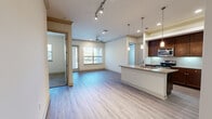 This two-story residence offers a thoughtfully designed layout across two floors, with the majority of the living space situated on the upper level. The open-concept main living area seamlessly connects the kitchen and living room, featuring light hardwood-style flooring, crown molding, track lighting, and a ceiling fan. Large windows invite abundant natural light and provide outdoor views, while a door leads to a private balcony. The kitchen is well-equipped with rich dark wood cabinetry, granite countertops, stainless steel appliances, a tile backsplash, and a peninsula with pendant lighting that offers additional prep and bar seating space. Built-in open shelving extends the kitchen's storage and display options. The primary bedroom is generously sized and includes a walk-in closet with built-in shelving and a full en-suite bathroom featuring a double vanity with granite countertops, a soaking tub, a separate glass-enclosed shower, and tile flooring. The second bedroom is carpeted, includes a ceiling fan, and has convenient access to its own bathroom. A dedicated laundry area houses a top-load washer with overhead shelving. The ground floor includes an attached garage with an automatic opener, providing secure parking and additional storage.