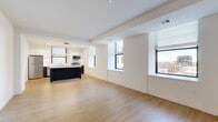 Located in the heart of Wilmington, Delaware, this modern 2-bedroom, 2-bathroom residence offers a thoughtfully designed open-concept layout with clean contemporary finishes throughout. Light wood flooring flows seamlessly across the entire unit, complementing the crisp white walls and creating a bright, cohesive aesthetic.

The open living area is spacious and filled with natural light from multiple large windows fitted with sleek blinds, offering sweeping views of the Wilmington cityscape. The kitchen is a standout feature, showcasing dark cabinetry with white quartz countertops, a large center island, stainless steel appliances including a refrigerator, range, microwave, and dishwasher, and pendant lighting overhead — all combining for a polished, functional workspace.

A clean hallway with recessed lighting connects the living areas to the two bedrooms, each of which is well-proportioned and bathed in natural light from city-facing windows. The generously sized primary bedroom offers ample space and multiple windows with urban views. Both bathrooms are finished with elegant herringbone-patterned grey tile flooring, white walls, dark vanities, and glass-enclosed showers. Two closets provide convenient storage throughout the unit.