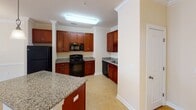 This single-floor residence offers a thoughtfully designed open-concept layout that seamlessly connects the kitchen and living areas, creating a cohesive and functional living environment. The kitchen is a standout feature, showcasing rich cherry wood cabinetry, speckled granite countertops, and a full suite of black appliances including a refrigerator, electric range, built-in microwave, and dishwasher. A peninsula counter adds additional prep space and serves as a natural divider between the kitchen and the adjoining living area. Crown molding throughout adds a refined architectural touch, lending an air of elegance to the neutral-toned interiors. The living and dining spaces are generously proportioned, with plush carpeting, ceiling fans, and a chandelier that contribute to a warm and inviting ambiance. Windows dressed with blinds allow natural light to filter in. Additional rooms, also carpeted and bathed in natural light, offer versatile functionality. The bathroom features a full tub and shower combination, a rich cherry wood vanity, and matching granite countertops that tie together the home's consistent design language. The overall aesthetic is clean, neutral, and move-in ready.