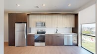 Located at 421 N Pennsylvania St in the heart of downtown Indianapolis, this modern one-bedroom, one-bathroom unit offers a well-designed layout across a single floor. The entrance leads into a bright hallway with light wood-style flooring and clean white walls, opening into an open-concept kitchen and living area. The kitchen is thoughtfully appointed with two-tone cabinetry — dark walnut lower cabinets paired with light upper cabinets — complemented by a white subway tile backsplash, light countertops, and a full suite of stainless steel appliances including a refrigerator, electric range, microwave, and dishwasher. Large floor-to-ceiling windows flood the living area with natural light and frame sweeping views of the Indianapolis skyline and surrounding urban landscape. The bedroom features plush carpeting, a built-in closet, and its own expansive window with city views. The bathroom is finished in a contemporary style with a walk-in glass-enclosed shower featuring matte black hardware, wood-toned cabinetry, and light flooring. Additional conveniences include two closets and an in-unit laundry area, rounding out this efficiently designed urban residence.