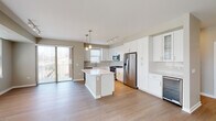 Located at 431 Melrose Ave in Glen Ellyn, Illinois, this single-floor residence presents a clean, contemporary design throughout. The open-concept kitchen serves as the centerpiece of the living area, featuring crisp white shaker cabinetry extending to the ceiling, a large central island with a white quartz countertop, and a full suite of stainless steel appliances including a gas range, built-in microwave, French door refrigerator, dishwasher, and a wine cooler. Pendant lighting and a track rail system illuminate the space, while light-toned hardwood flooring flows seamlessly through the kitchen and into the adjoining living area. A sliding glass door provides direct access to an outdoor balcony, allowing natural light to pour in. The bedrooms offer a calm, neutral palette with light hardwood floors and multiple windows fitted with blinds. One bedroom features angled ceiling detail, adding architectural interest. The walk-in closet is generously proportioned, finished with carpet and wire shelving systems for organized storage. The bathrooms are well-appointed with white shaker vanities, quartz countertops, large mirrors, and tile flooring. The primary bath includes a spacious walk-in shower with sliding glass doors, contributing to the unit's polished, move-in-ready presentation.