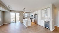 Located at 431 Melrose Ave in Glen Ellyn, Illinois, this single-floor residence presents a clean, contemporary design throughout. The open-concept kitchen serves as the centerpiece of the living area, featuring crisp white shaker cabinetry extending to the ceiling, a large central island with a white quartz countertop, and a full suite of stainless steel appliances including a gas range, built-in microwave, French door refrigerator, dishwasher, and a wine cooler. Pendant lighting and a track rail system illuminate the space, while light-toned hardwood flooring flows seamlessly through the kitchen and into the adjoining living area. A sliding glass door provides direct access to an outdoor balcony, allowing natural light to pour in. The bedrooms offer a calm, neutral palette with light hardwood floors and multiple windows fitted with blinds. One bedroom features angled ceiling detail, adding architectural interest. The walk-in closet is generously proportioned, finished with carpet and wire shelving systems for organized storage. The bathrooms are well-appointed with white shaker vanities, quartz countertops, large mirrors, and tile flooring. The primary bath includes a spacious walk-in shower with sliding glass doors, contributing to the unit's polished, move-in-ready presentation.