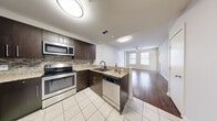 This well-appointed single-floor residence offers a thoughtfully designed open-concept layout that seamlessly connects the kitchen and living areas. The kitchen is a standout feature, equipped with dark espresso cabinetry, granite countertops, a mosaic tile backsplash, and a full suite of stainless steel appliances including a French door refrigerator with ice maker, electric range, built-in microwave, and dishwasher. A black matte gooseneck faucet anchors the undermount double sink, which sits atop a peninsula that serves as a natural divider between the kitchen and living space. Rich, warm-toned hardwood flooring flows throughout the living areas and bedrooms, contrasting beautifully with the light ceramic tile in the kitchen. The living area benefits from natural light streaming through multiple windows fitted with horizontal blinds and is completed by a ceiling fan. A hallway leads to the bedrooms and bathroom, each room featuring the same warm hardwood floors and generous window placement that invites abundant natural light. The bathroom presents dark espresso cabinetry with a granite-topped vanity and a large mirror. Neutral wall tones and clean architectural lines give the space a modern, cohesive aesthetic throughout.