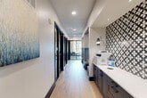 Located at 6735 Standifer Gap Rd in Chattanooga, TN, this single-floor business center offers a generously sized, thoughtfully designed environment tailored for productivity and professional use. The central hallway serves as the spine of the space, finished with light wood-look flooring and recessed lighting that creates a clean, bright atmosphere throughout.

Along the hallway, a built-in service station features dark cabinetry with white countertops and a striking black-and-white patterned tile accent wall, providing a functional print and work area. Adjustable wall-mounted sconces add focused task lighting, while curated artwork enhances the visual appeal.

Multiple private workspaces and a dedicated conference room line the corridor, each enclosed by sleek black-framed glass doors that maintain an open, transparent feel while ensuring acoustic privacy. The conference room is distinguished by exposed wood beam accents, carpeted flooring, and large windows that invite natural light and views of the surrounding exterior. Individual workspaces feature a mix of carpet and wood-look flooring, wood paneling details, and ample room for focused work or small meetings.

The overall design balances contemporary aesthetics with practical functionality, incorporating a cohesive palette of navy blue, charcoal, white, and natural wood tones. The space projects a polished, professional ambiance well-suited for collaborative or independent work.