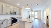 Located in Jacksonville, FL, this well-appointed 2-bedroom, 2-bathroom residence offers a thoughtfully designed single-floor layout with modern finishes throughout. The open-concept kitchen and living area serves as the heart of the home, anchored by a large granite-topped island with an undermount sink and matte black faucet, illuminated by stylish pendant lights with gold accents. The kitchen is fully equipped with gray shaker-style cabinetry, stainless steel appliances including a French door refrigerator, electric range, and built-in microwave, all set against a herringbone tile backsplash and light hardwood-style flooring. Natural light pours in through large windows and a glass door leading to a private balcony, creating a bright and airy atmosphere. The primary bedroom is generously sized with plush carpet flooring, a ceiling fan, and an expansive walk-in closet outfitted with multi-level wire shelving. The en-suite bathroom features granite countertops, gray cabinetry with matte black hardware, and a glass-enclosed walk-in shower. The second bathroom offers a full tub-shower combo with subway tile surround. In-unit laundry is also included, adding everyday convenience to this refined Jacksonville residence.