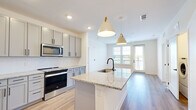 Located in Jacksonville, FL, this well-appointed 2-bedroom, 2-bathroom residence offers a thoughtfully designed single-floor layout with modern finishes throughout. The open-concept kitchen and living area serves as the heart of the home, anchored by a large granite-topped island with an undermount sink and matte black faucet, illuminated by stylish pendant lights with gold accents. The kitchen is fully equipped with gray shaker-style cabinetry, stainless steel appliances including a French door refrigerator, electric range, and built-in microwave, all set against a herringbone tile backsplash and light hardwood-style flooring. Natural light pours in through large windows and a glass door leading to a private balcony, creating a bright and airy atmosphere. The primary bedroom is generously sized with plush carpet flooring, a ceiling fan, and an expansive walk-in closet outfitted with multi-level wire shelving. The en-suite bathroom features granite countertops, gray cabinetry with matte black hardware, and a glass-enclosed walk-in shower. The second bathroom offers a full tub-shower combo with subway tile surround. In-unit laundry is also included, adding everyday convenience to this refined Jacksonville residence.