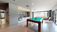 Located at 455 West Ave in Norwalk, Connecticut, this expansive amenity lounge offers a thoughtfully designed, multi-functional space that blends entertainment and relaxation in a contemporary setting. The single-floor layout is anchored by polished concrete flooring that flows seamlessly throughout, lending an industrial-chic aesthetic to the overall design.

The space is divided into distinct activity zones. A dedicated golf simulator area features artificial turf and a projection setup, framed by dramatic floor-to-ceiling curtains for an immersive experience. Adjacent to this, a game room houses a full-size pool table, a shuffleboard table, a foosball table, and a ping-pong table, all set beneath recessed lighting on gleaming polished floors.

A comfortable lounge area is defined by generous sectional sofas, accent chairs, and a stylish coffee table, bathed in abundant natural light from expansive floor-to-ceiling windows that frame dynamic views of the surrounding Norwalk streetscape. Black-framed glass partitions elegantly separate the lounge from the game zones while maintaining a sense of openness.

A built-in wet bar and kitchenette with light wood cabinetry, open shelving, and counter space provides convenient refreshment access. A wall-mounted television enhances the entertainment offering. The overall ambiance is modern, social, and inviting, making this a premier gathering space for its community.