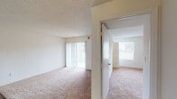 This single-floor residential unit offers a practical and well-organized layout designed for comfortable everyday living. The open-concept kitchen and adjoining living and dining area form the heart of the space, connected by a peninsula breakfast bar with a built-in sink. The kitchen is equipped with ample light wood cabinetry, black appliances including a gas range, refrigerator, and dishwasher, and is illuminated by a combination of overhead fluorescent and pendant lighting. Dark hardwood-style flooring flows throughout the kitchen, dining, and hallway areas, creating a clean contrast with the neutral white walls.

The living room features plush carpeting, a textured ceiling, and a sliding glass door fitted with vertical blinds that opens to an outdoor patio, allowing natural light to fill the space. Multiple bedrooms continue the carpeted flooring theme and are bathed in natural light through windows with outdoor views. Each bedroom includes closet storage, with at least one featuring a louvered bifold closet door.

Two bathrooms serve the unit — one with a tub-shower combination and tile surround, and another with a vanity and toilet. Both feature dark hardwood-style flooring consistent with the common areas. Overall, the unit presents a clean, neutral palette throughout, offering a functional and move-in ready living environment.