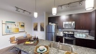 This single-floor residence offers a thoughtfully designed open-concept layout that seamlessly connects the kitchen and dining areas, creating a cohesive and functional living environment. The kitchen is a standout feature, showcasing rich dark-toned cabinetry that contrasts elegantly with the speckled granite countertops. Stainless steel appliances, including a French door refrigerator, electric range, and over-the-range microwave, provide a sleek and contemporary finish. A deep undermount sink with a modern faucet sits at the kitchen island, which also serves as a natural gathering point for casual dining or entertaining. Stylish pendant lights hang above the island, complementing the track lighting that runs throughout the space and ensures excellent illumination in every corner. A mosaic tile backsplash adds a subtle decorative accent to the kitchen. The adjacent dining area is bright and inviting, with white walls adorned with framed artwork that adds a touch of personality. Crown molding along the ceiling elevates the overall finish of the space, lending it a polished and refined character. The open flow between the kitchen and dining areas makes this residence well-suited for both everyday living and entertaining guests.