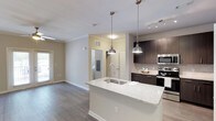 This well-appointed single-floor residence at 3130 Hillandale Rd in Durham, NC offers a thoughtfully designed layout with modern finishes throughout. The open-concept kitchen is a standout feature, showcasing dark espresso cabinetry reaching to the ceiling, granite-look countertops, a subway tile backsplash, and a full suite of stainless steel GE appliances including a gas range, over-the-range microwave, and side-by-side refrigerator with ice and water dispenser. A large kitchen island with a built-in sink and stylish pendant lighting anchors the space, with convenient access to a well-organized walk-in pantry nearby. The kitchen flows seamlessly into the living area, which is adorned with wood-look flooring, crown molding, a ceiling fan, and French doors that open to a private balcony with outdoor views. Bedrooms feature plush carpeting and ceiling fans, with the primary bedroom offering a walk-in closet and direct access to a private bath. The bathroom is finished with granite-look counters, dark cabinetry, a large mirror, and a full tub-shower combination. A dedicated laundry room houses a full-size top-loading washer and dryer with additional wire shelving for storage. Neutral tones and clean lines lend the entire space a bright, modern ambiance.